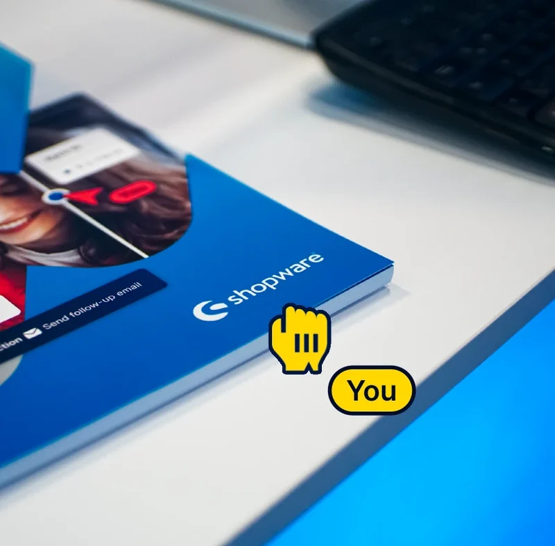 Shopware brand brochure beside a laptop, with a yellow hand pointer and You label.